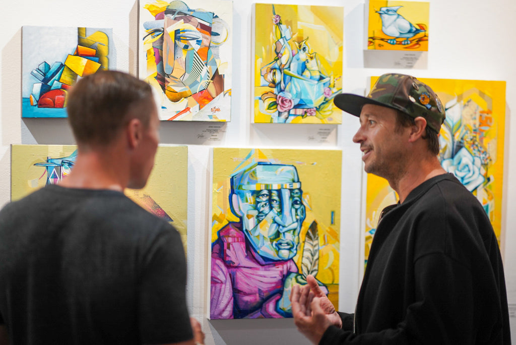 Photograph of two men looking at artwork during the opening of the "Reflect.Renew.Rebirth" duo exhibition at Voss Gallery in San Francisco, July 21, 2023.