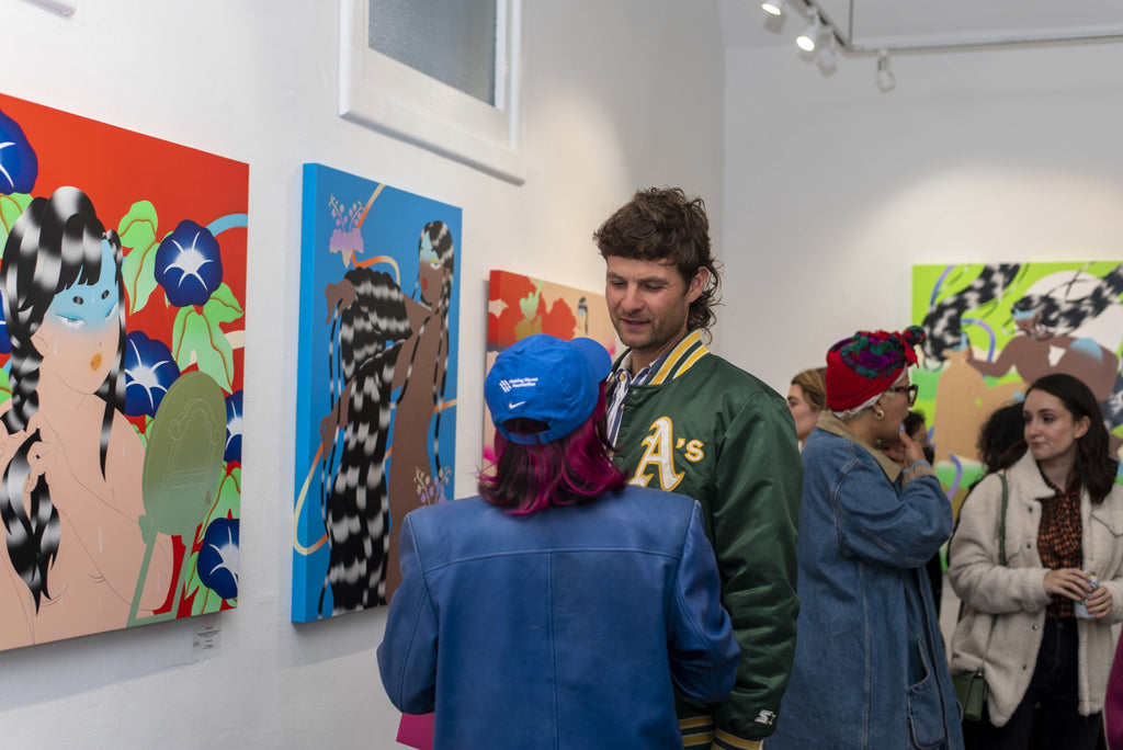 Photograph of two people talking in front of artwork during Maya Fuji's "Kami" solo exhibition Opening Reception at Voss Gallery in San Francisco, May 27, 2022.