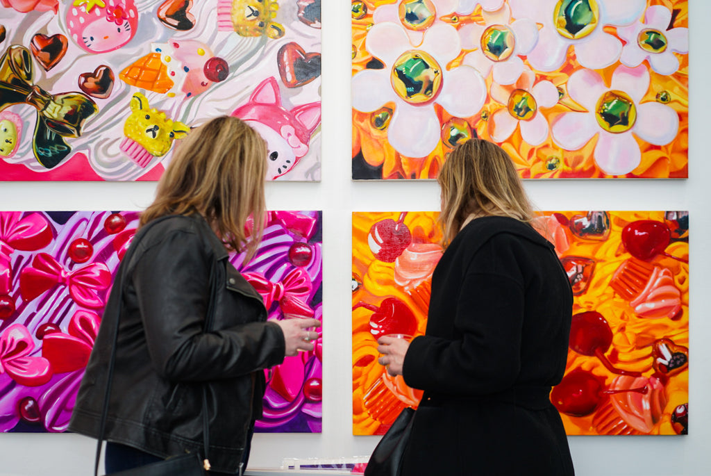 Two women in casual attire viewing vibrant, colorful abstract paintings at an art exhibition, reflecting the engaging and dynamic atmosphere of Voss Gallery, San Francisco.