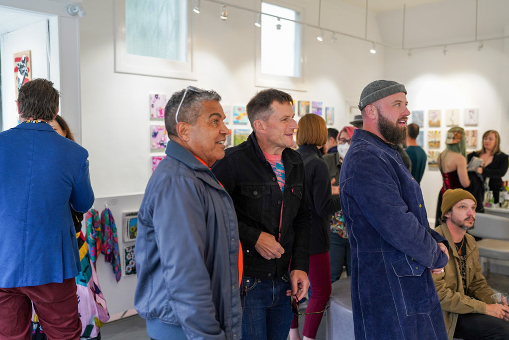 Photograph of people looking at artwork during the Postcards from Paradise Juried Group Exhibition Opening Reception at Voss Gallery in San Francisco, May 26, 2023.