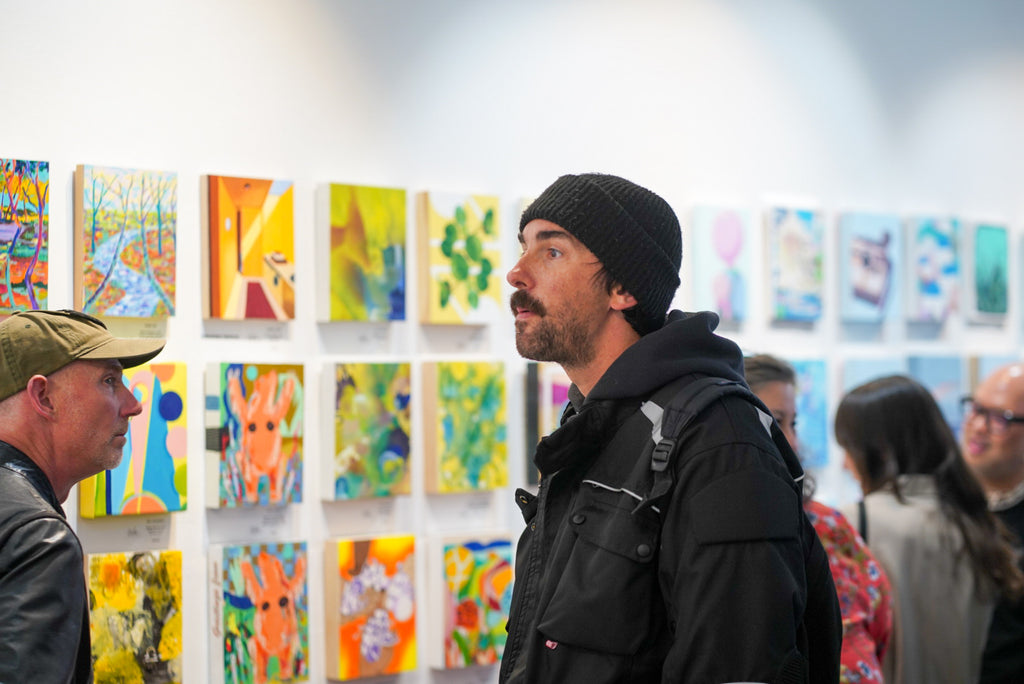 Photograph of a man wearing a bonnet and some guests during the Opening Reception of the Postcards from Paradise Juried Group Exhibition at Voss Gallery in San Francisco, May 26, 2023.