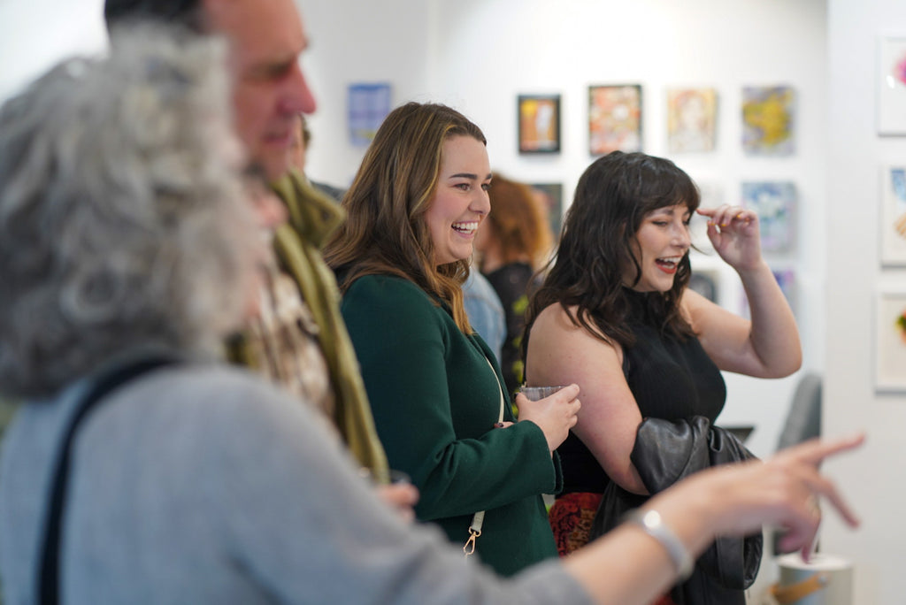 Photograph of people smiling and viewing artwork during the Opening Reception of the Postcards from Paradise Juried Group Exhibition at Voss Gallery in San Francisco, May 26, 2023.