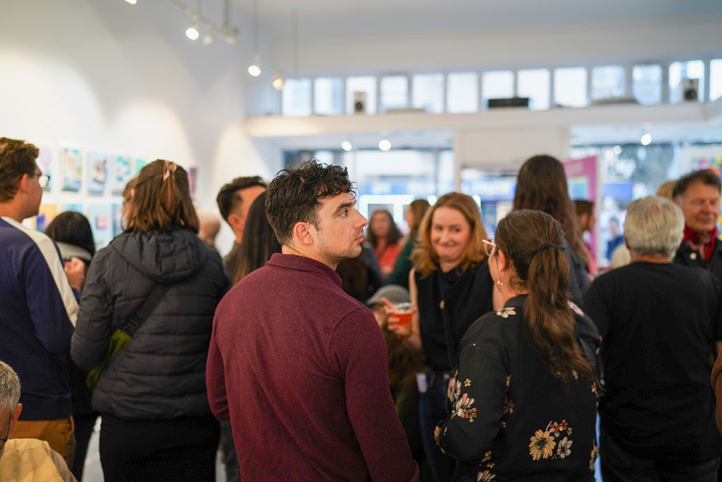 Photograph of people attending and celebrating the Postcards from Paradise Juried Group Exhibition Opening Reception at Voss Gallery in San Francisco, May 26, 2023.