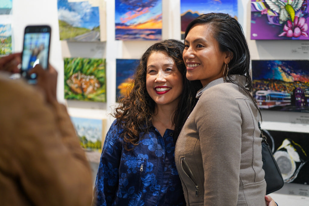 Photograph of two ladies smiling during the Postcards from Paradise Juried Group Exhibition Opening Reception at Voss Gallery in San Francisco, May 26, 2023.