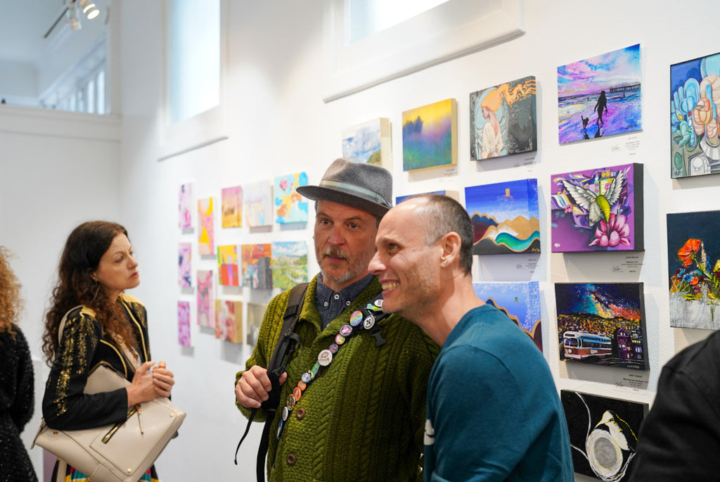 Photograph of gallery visitors viewing artwork during the Postcards from Paradise Juried Group Exhibition Opening Reception at Voss Gallery in San Francisco, May 26, 2023.