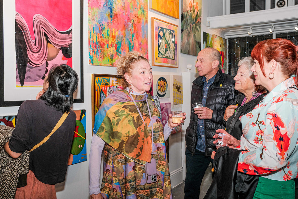 Photograph of people with drinks viewing art and talking during the "Refusés of the Bay" Group Exhibition Opening Reception at Voss Gallery, San Francisco, September 29, 2023.