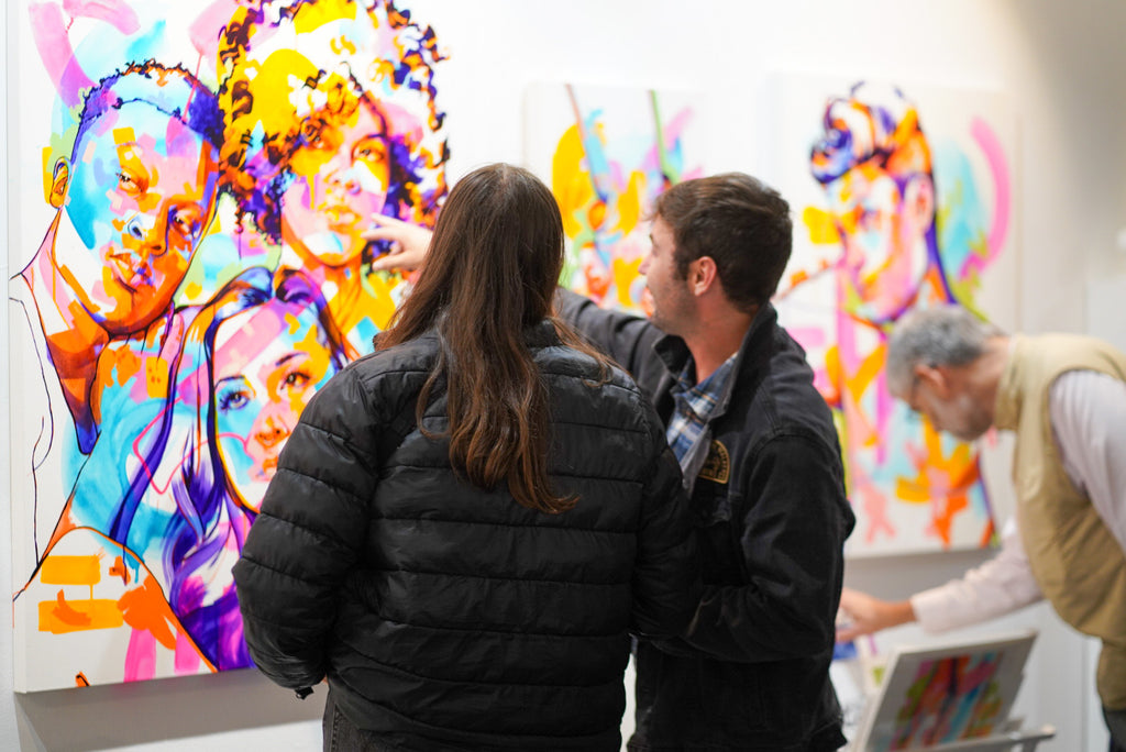 Photograph of two people looking at artwork on the wall during the The Tracy Piper's "All the Feels" solo exhibition opening reception at Voss Gallery, San Francisco, August 25, 2023.