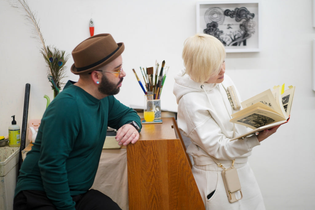 Photograph of two artists browsing an art book during the 'Art Unveiled: Collectors Mixer' at Voss Collector Club's visit to 1890 Bryant Studios, San Francisco, on March 10th, 2024.