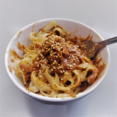 Noodles with peanut sauce and garnished with sesame seeds.