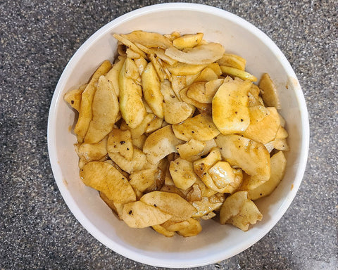 Apple slices in a bowl that have been tossed with the spice and sugar mixture.