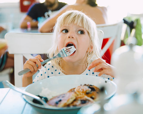 Little girl enjoying a plate of blueberry pancakes with cream.