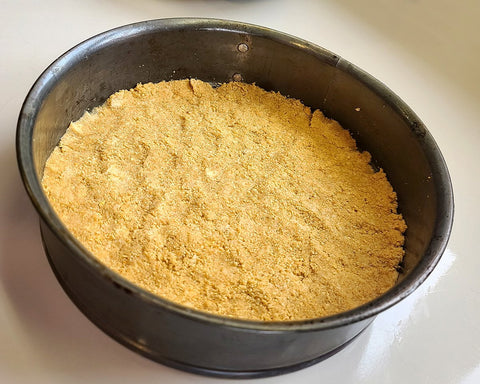 Graham cracker crumbs pressed into the bottom of a spring form pan to make the foundation for the cheesecake.