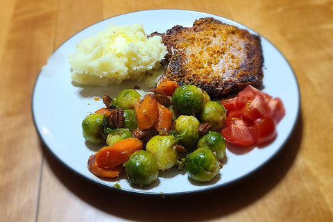 Plated dinner of roasted veggies, pork chops, mashed potatoes and cherry tomatoes.