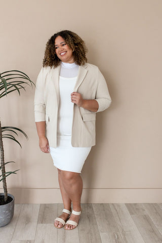 A woman wearing a white dress and tan blazer, showcasing crop top layering with a halftee for a stylish look