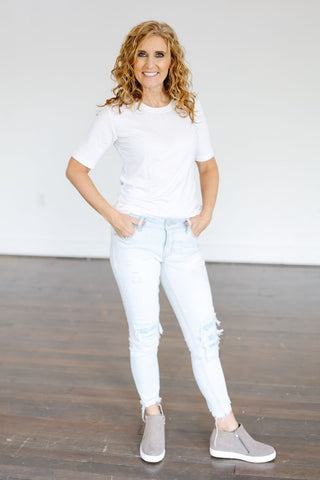 A woman wearing a white t-shirt and ripped jeans, showcasing a trendy crop top layering style