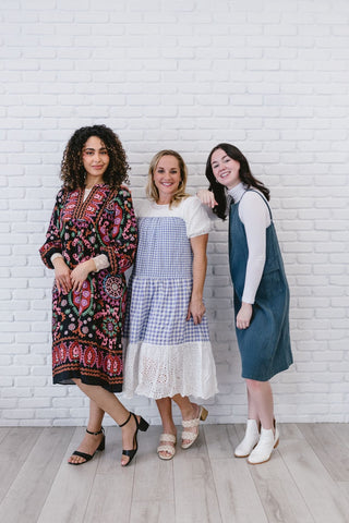 Three women in modest clothing standing in front of a white brick wall, showcasing Half Tank fashion