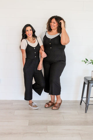 Two women in black overalls standing next to each other, showcasing crop top layering fashion trend