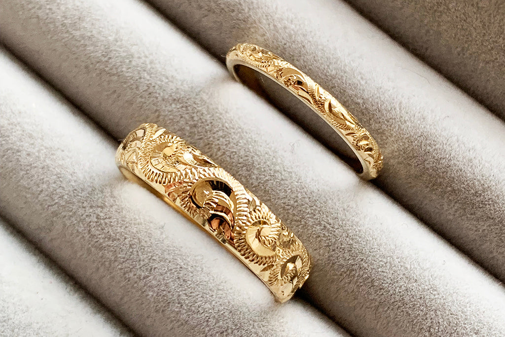 His and hers ethical gold wedding bands - one 2mm wide and the other 5mm wide - both hand engraved with intricate scrolls