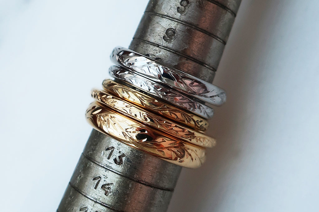 A series of ethical gold wedding bands in various widths, stacked on a ring sizing rod, hand engraved with vines