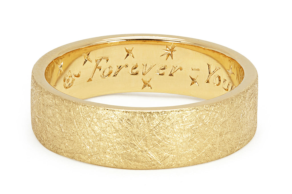 A bespoke Fairtrade Gold wedding band with a flat profile and distressed finish, hand engraved with a romantic message on the inside