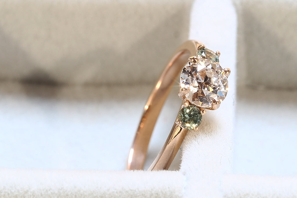 A client's bespoke trilogy engagement ring catching the sunshine. An 18ct sustainable recycled rose gold band is set with the client's own reclaimed vintage old European cut diamond and traceable conflict-free green sapphires