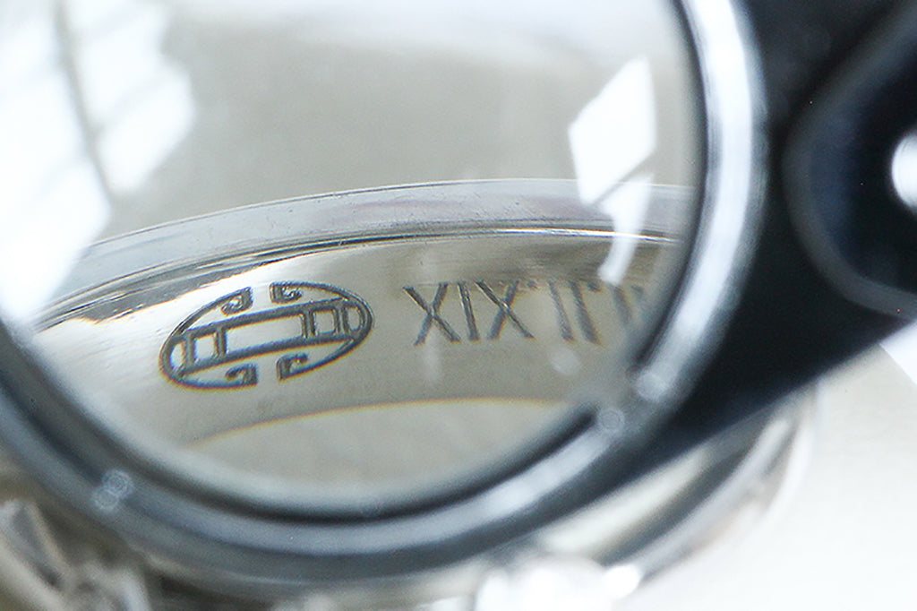 The inside of a platinum wedding band as seen through a loupe, magnifying a geometric laser engraved emblem