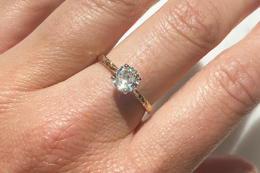 An ethical engagement ring cast in eco recycled gold, hand engraved with scrolls and set with an antique old cut diamond - modelled on a woman's hand