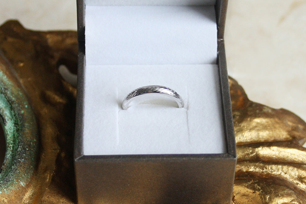 A recycled platinum wedding band hand engraved with a wheat sheaf pattern, sat inside a recyclable ring box