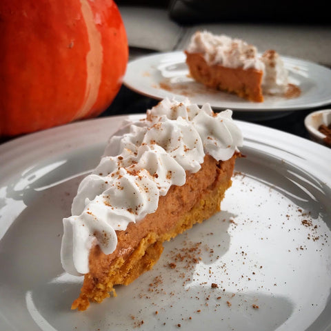 Two pieces of Shanti Chai Pumpkin Pie topped with coconut cream, in front of a winter squash. 