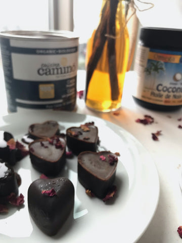 Vanilla and Rose Petal Chocolates on a white plate in front of a bottle of homemade vanilla extract, coconut oil and organic cocoa.