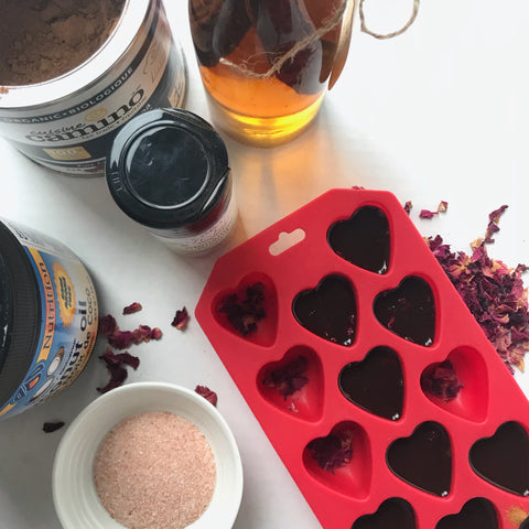 Pouring warmed chocolate mix into mold, with vanilla extract, cinnamon, coconut oil, Himalayan salt and organic cocoa in the background.