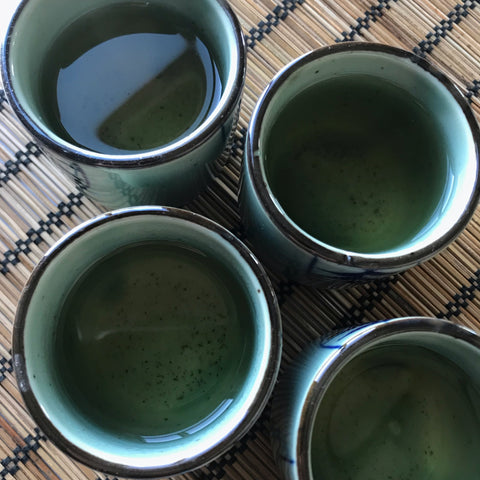 Four tiny cups of Sencha Green Tea atop a bamboo placemat, ready to be enjoyed with friends. 