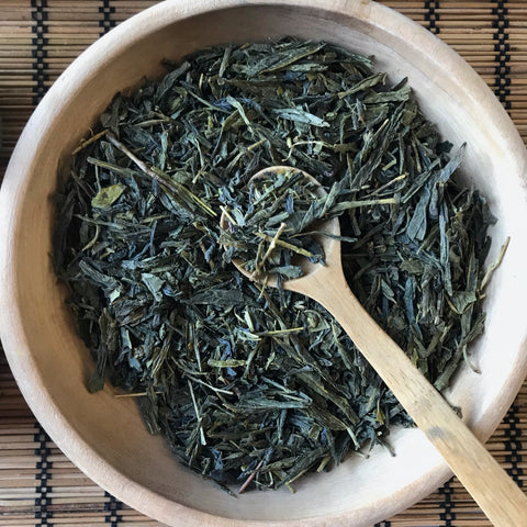 Shanti Chai & Co's Sencha Green Tea in a wooden bowl with a wooden teaspoon, perfect for measuring out enough green tea leaves for one cup of tea.