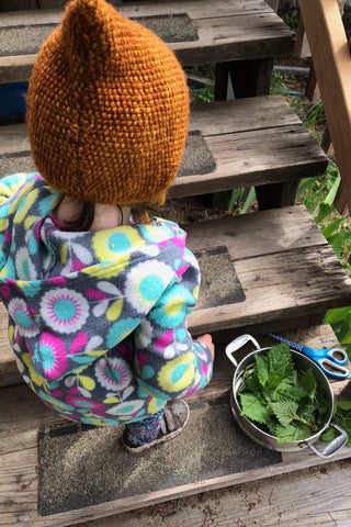 A small child stands on the stairs next to some freshly picked herbs.