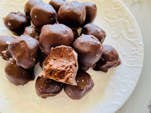 A stack of elderberry chocolate truffles with a bite taken out of one sitting on a plate.