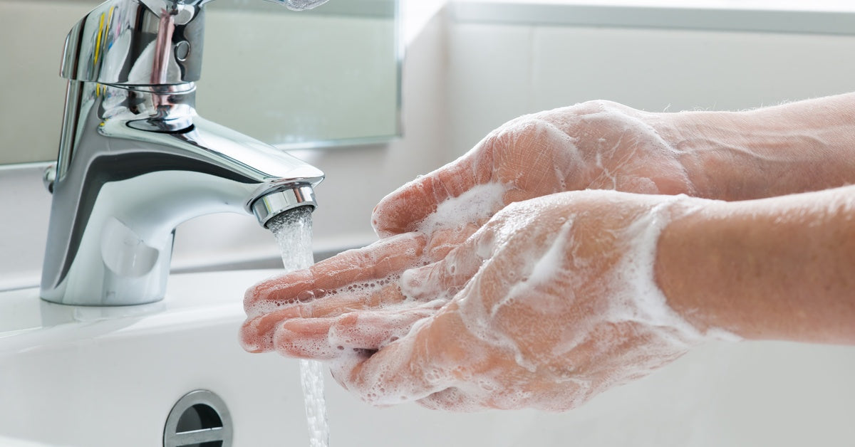 A person lathers their hands with soap and prepares to rinse them under a running faucet in a bathroom.