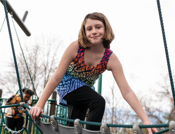 Evie playing on the playground wearing the rainbow rhino tank dress