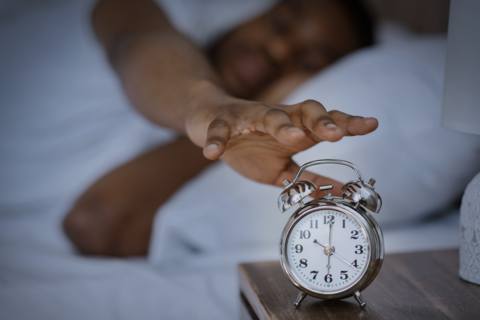man turning off alarm clock in bed