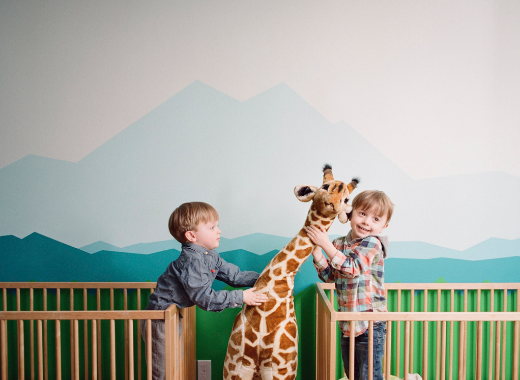 Kim Hildebrand's lifestyle photograph of twin boys in their cribs sharing their giraffe toy