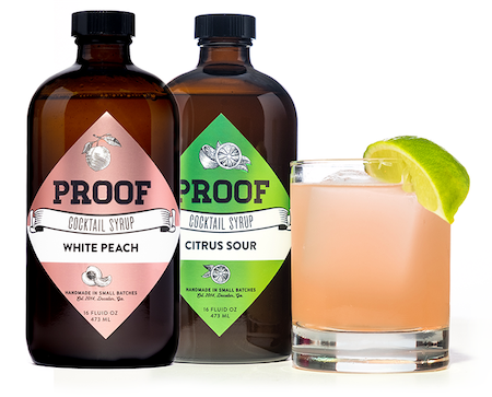 bottles of White Peach and Citrus Sour Proof Syrup next to a cocktail