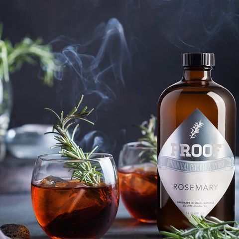 a pair of rosemary Negroni cocktails sit alongside a bottle of Rosemary Proof Syrup