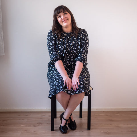 Bri pictured seated wearing black floral Forget-me-not Valerie Raglan Dress