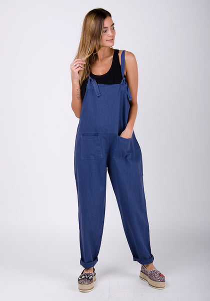 Blue linen dungaree all-in-one jumpsuit for women with hand in left pocket.