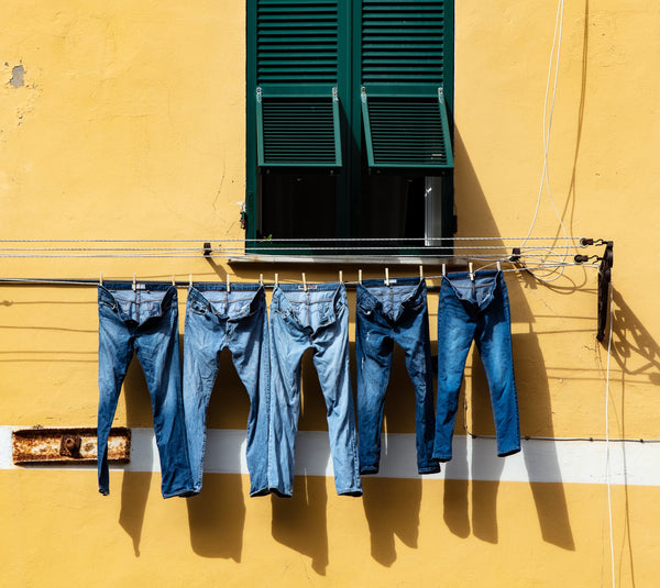 Five pairs of jeans drying on a line outdoors.