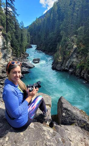 Photographer sitting on a cliff edge overlooking a teal blue river in British Columbia, Canada