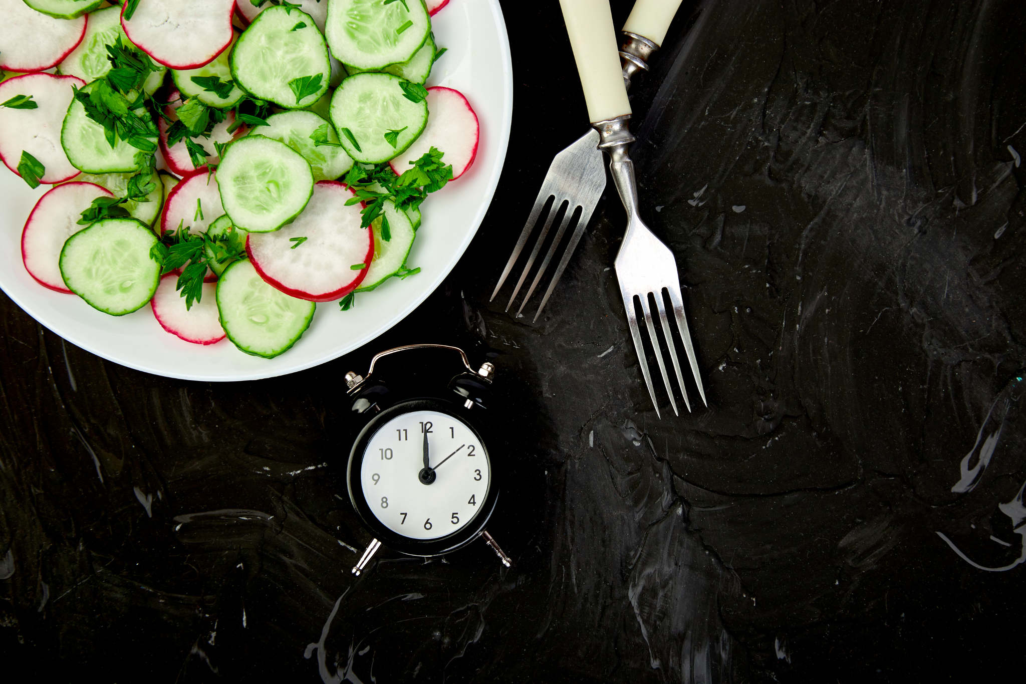 Assiette de radis et concombre avec un chronomètre à côté et des couverts pour montrer qu'il y a une heure de la journée pour chaque aliment
