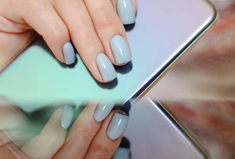 Two pretty hands manicured with blue-gray pastel polish on pretty long nails holding a cell phone with the same shades