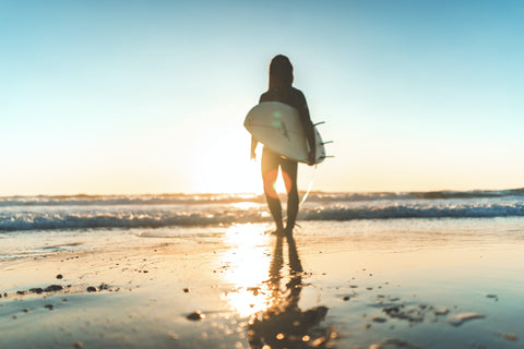 Une personne se balade sur la plage avec son surf sous le bras