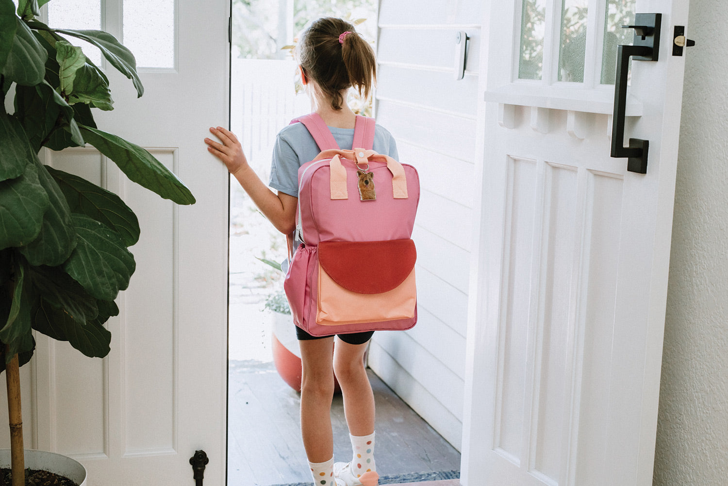 school girl walking out the door to school with pink school bag and quokka key chain 