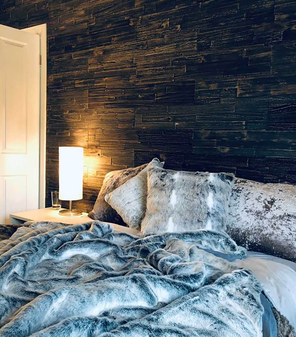 Black wooden wall panel planks behind a bed with blue blankets
